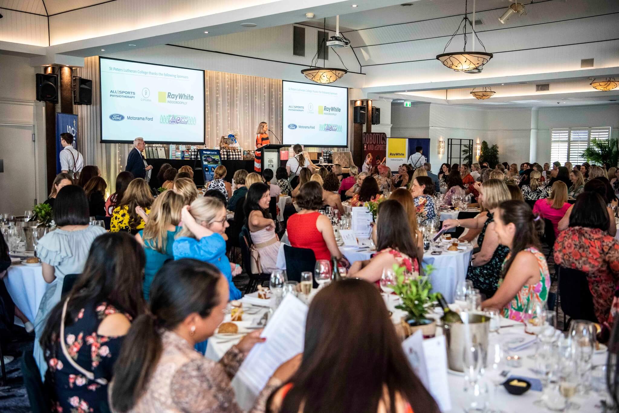 Corporate gathering with guests and speaker on stage inside a large event venue in Brisbane
