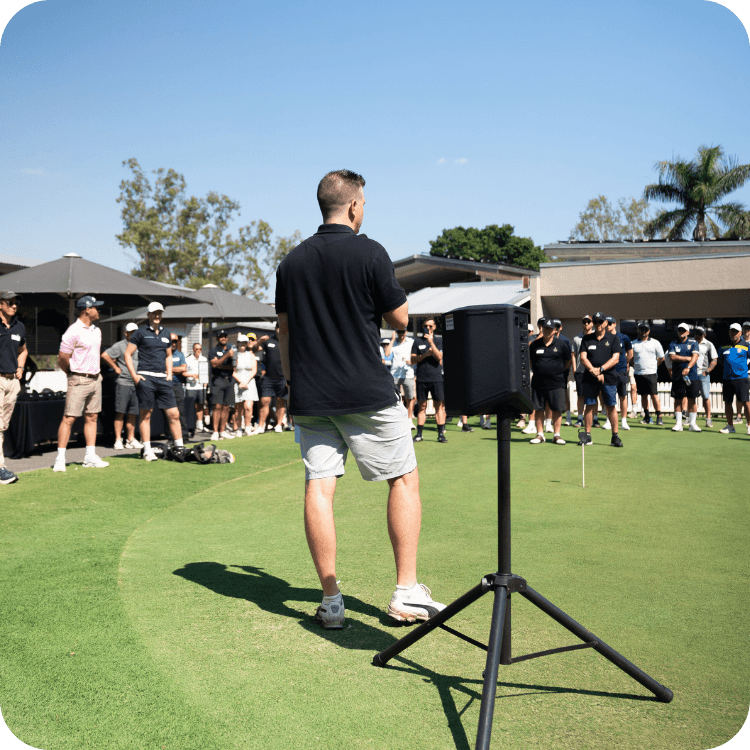 A man presenting to a crowd of people on the putting green at St Lucia Golf Links in Brisbane.